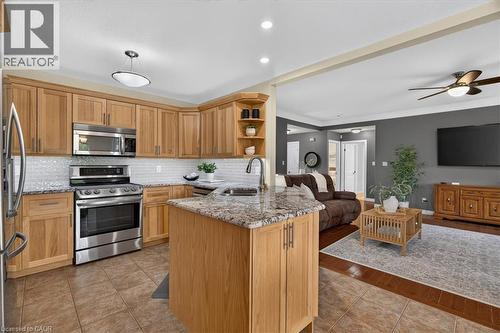 Open-concept kitchen with wood-finish cabinetry, stainless steel appliances, granite countertops, and tile flooring - 515 Woodward Drive, Mount Brydges, ON 