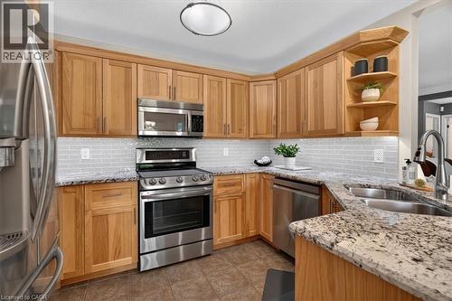 Kitchen featuring wood cabinetry, stainless steel appliances, speckled stone countertops, a subway tile backsplash, and a double basin sink - 515 Woodward Drive, Mount Brydges, ON 