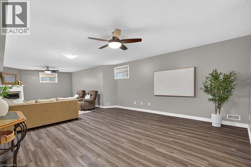 Spacious room featuring wood-finish flooring, two ceiling fans with integrated lighting, multiple windows, and a white fireplace - 515 Woodward Drive, Mount Brydges, ON 