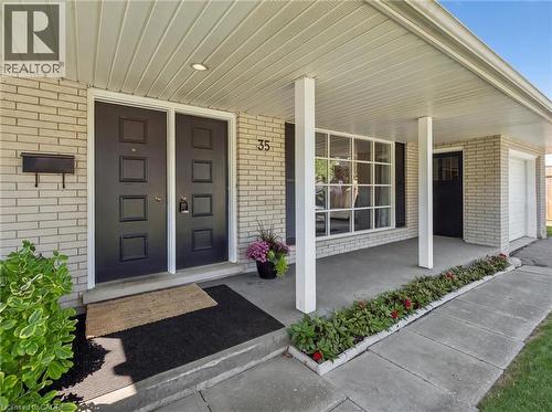 Light-colored brick exterior with a covered porch, featuring dual black entry doors with square paneling, a large multi-pane window, and a white garage door - 35 Crosby Drive, Kitchener, ON 