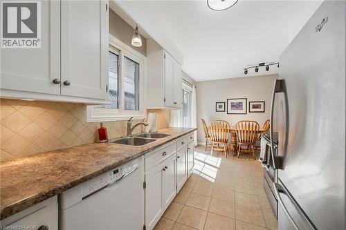 Kitchen featuring white cabinetry, a double basin sink with a gooseneck faucet, a tile backsplash, and a built-in dishwasher - 35 Crosby Drive, Kitchener, ON 