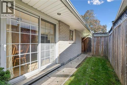 Sliding glass door with grid detailing, brick exterior, covered patio, wooden privacy fence, and a wooden gate - 35 Crosby Drive, Kitchener, ON 