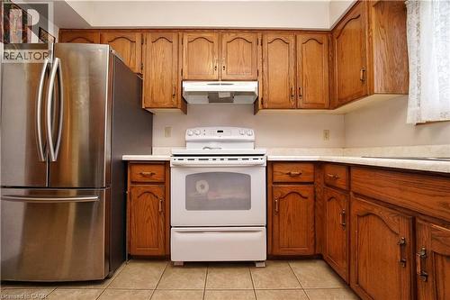 Wood cabinetry with brass hardware, white countertops, stainless steel French door refrigerator, white electric range with hood, and tile flooring - 56 Scenic Wood Crescent, Kitchener, ON 