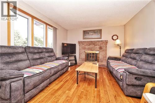 Warm living area featuring wood-finish flooring, a brick fireplace, and large windows with wood trim - 56 Scenic Wood Crescent, Kitchener, ON 