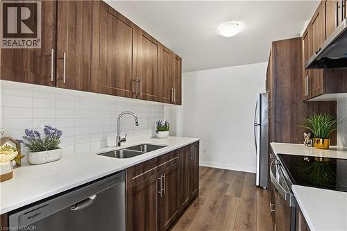 Kitchen featuring dark wood-finish cabinetry, stainless steel appliances, a double basin sink, white countertops, and a subway tile backsplash - 1444 Upper Ottawa Street Unit# 32, Hamilton, ON 