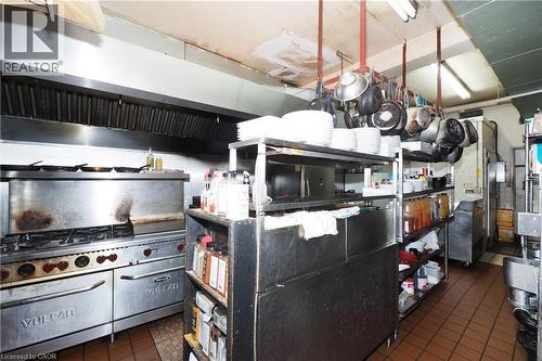 Commercial kitchen featuring a stainless steel range with a ventilation hood, tiled flooring, and extensive metal shelving - 707 E King Street E, Cambridge, ON 