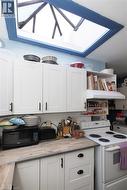 Kitchen featuring white shaker-style cabinetry, wood-finish countertops, a white subway tile backsplash, and a large skylight - 