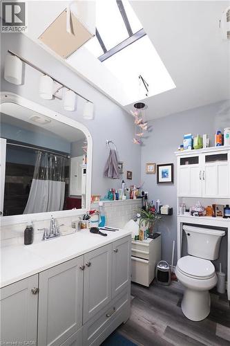 Skylight and ceiling-mounted light fixture, wood-finish flooring, vanity with a white countertop, chrome faucet, and white cabinetry - 707 E King Street E, Cambridge, ON 
