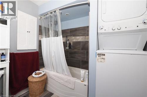 Tub with tiled surround and recessed shelf, wood-finish flooring, and a stacked washer and dryer unit - 707 E King Street E, Cambridge, ON 