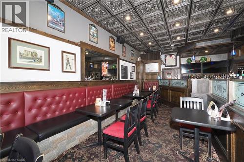 Pressed tin ceiling with recessed lighting, built-in banquette seating with tufted backrests, stone veneer wall accents, wood paneling, and a full-service bar area - 707 E King Street E, Cambridge, ON 