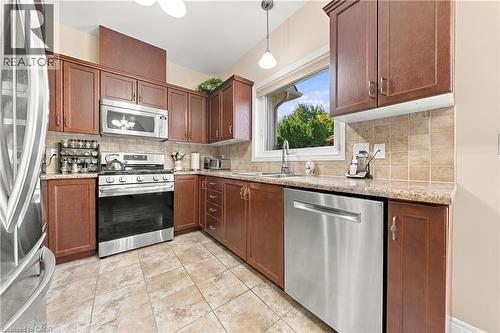 Kitchen featuring stainless steel appliances, wood-finish cabinetry, tile flooring, and a window above the sink - 31 Book Road Unit# 44, Grimsby, ON 