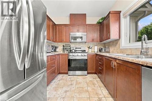 Stainless steel French door refrigerator, wood cabinetry, tile backsplash, stainless steel gas range, and a window above the sink - 31 Book Road Unit# 44, Grimsby, ON 