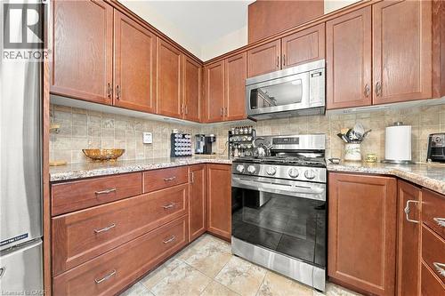 Rich wood-finish cabinetry, stainless steel appliances, patterned tile flooring, speckled countertops, and a tiled backsplash - 31 Book Road Unit# 44, Grimsby, ON 