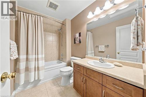 Bathroom featuring a vanity with an oval sink, wall-mounted light fixture, full-width mirror, a tub/shower combination with tile surround, and tile flooring - 31 Book Road Unit# 44, Grimsby, ON 