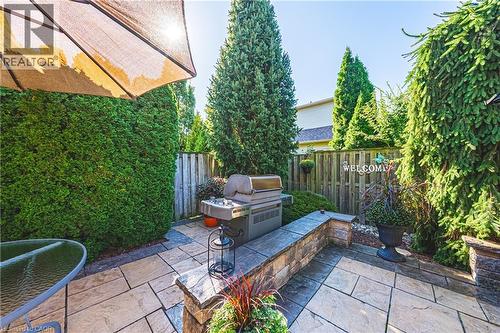 Patio area featuring stone tile hardscaping, built-in stone wall, privacy fencing, and mature evergreen plantings - 31 Book Road Unit# 44, Grimsby, ON 