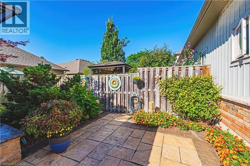 Patio area featuring stone pavers, a wooden fence, surrounding landscaping, and brick and siding exterior - 31 Book Road Unit# 44, Grimsby, ON 