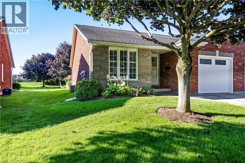 Brick and stone-finish exterior featuring a single garage, front entry, and mature landscaping - 150 Oak Street Unit# 27, Simcoe, ON 