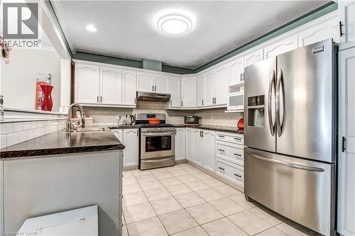 White cabinetry, stainless steel appliances, dark countertops, tile backsplash, and tile flooring - 150 Oak Street Unit# 27, Simcoe, ON 