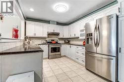 White cabinetry, stainless steel appliances, dark countertops, tile backsplash, and tile flooring - 