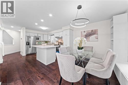 Dark wood-finish flooring throughout, white kitchen cabinetry with stainless steel appliances, and a kitchen island with a light-colored countertop - 495 Brigantine Drive, Waterloo, ON 