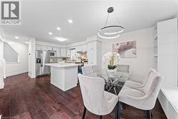 Dark wood-finish flooring throughout, white kitchen cabinetry with stainless steel appliances, and a kitchen island with a light-colored countertop - 