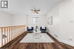 Wood-finish flooring, light-toned wall paint, wood railing, window with blinds, and a ceiling fan - 