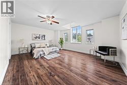 Wood-finish flooring throughout, multiple windows providing natural light, a ceiling fan with integrated lighting, and white baseboards - 