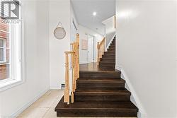 Dark wood-finish staircase with light wood railings, white walls, and ceramic tile flooring - 