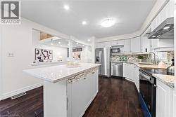 Kitchen featuring a central island with a light-toned countertop, white cabinetry, dark wood-finish flooring, stainless steel appliances, and a tiled backsplash - 