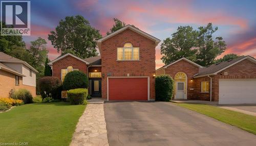 Brick exterior with arched window details, attached garage, paved driveway, and stone-accented walkway - 26 Stanmore Avenue, Kitchener, ON 