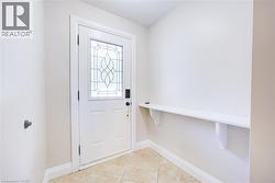 Entryway featuring a white door with decorative glass inserts, ceramic tile flooring, a built-in shelf, and neutral wall tones - 