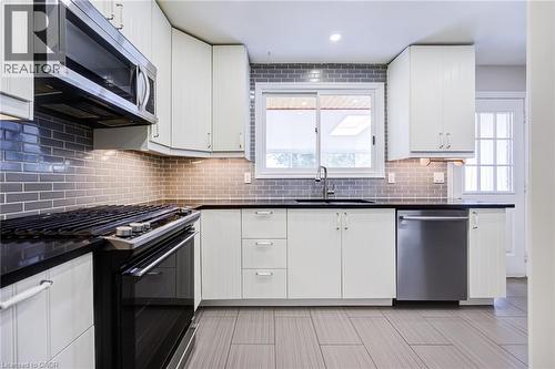Stainless steel microwave, black electric range, gray subway tile backsplash, white cabinetry, and a stainless steel dishwasher - 2037 Mountain Grove Avenue, Burlington, ON 