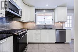 Stainless steel microwave, black electric range, gray subway tile backsplash, white cabinetry, and a stainless steel dishwasher - 