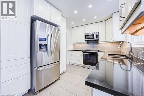 Stainless steel appliances, black countertops, white shaker-style cabinetry, subway tile backsplash, and light-toned tile flooring - 2037 Mountain Grove Avenue, Burlington, ON 