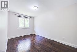 Rich wood-finish flooring, white walls, and a single window with white trim - 