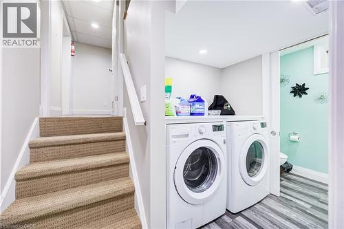 Carpeted staircase with white handrail, recessed lighting, and laundry area featuring front-loading washer and dryer - 2037 Mountain Grove Avenue, Burlington, ON 
