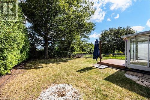 Expansive grassy yard with mature trees, a wooden deck, and a sunroom featuring large glass sliding doors - 2037 Mountain Grove Avenue, Burlington, ON 