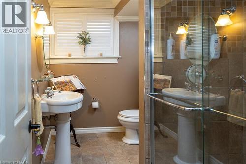 Pedestal sink with chrome fixtures, wall-mounted light fixtures, tile flooring, and a glass-enclosed shower - 78 Berkley Crescent, Simcoe, ON 