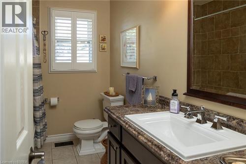 White plantation shutters, full vanity with integrated sink, chrome dual-handle faucet, dark wood-finish vanity cabinetry, and a walk-in shower with brown tile surround - 78 Berkley Crescent, Simcoe, ON 