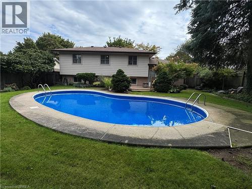 In-ground swimming pool with an oval shape, surrounded by a concrete border and grass landscaping - 78 Berkley Crescent, Simcoe, ON 