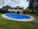 In-ground swimming pool with an oval shape, surrounded by a concrete border and grass landscaping - 78 Berkley Crescent, Simcoe, ON 