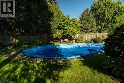 Backyard featuring a covered in-ground pool, expansive lawn, stone paving, privacy fencing, and mature perimeter trees - 78 Berkley Crescent, Simcoe, ON 