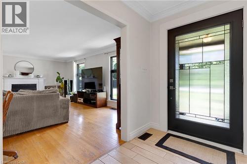 Entry door with decorative glass panels, crown molding, wood-finish flooring, white fireplace with mantel, and recessed lighting - 7 Shadywood Lane, Cambridge, ON 