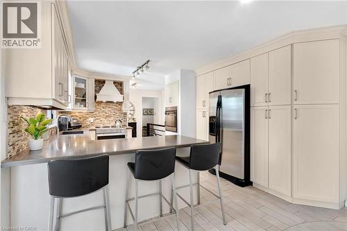 Kitchen featuring extensive cabinetry, a built-in range hood, a stainless steel refrigerator, a large counter-height island, and wood-finish flooring - 7 Shadywood Lane, Cambridge, ON 