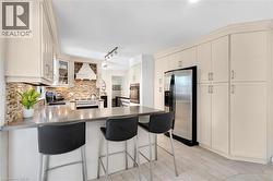 Kitchen featuring extensive cabinetry, a built-in range hood, a stainless steel refrigerator, a large counter-height island, and wood-finish flooring - 