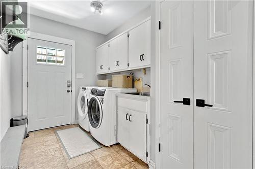 Utility area featuring white paneled cabinetry, front-load washer and dryer, and a built-in sink with a countertop - 7 Shadywood Lane, Cambridge, ON 