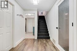 Wood-finish flooring, white paneled walls, black staircase, recessed lighting, and a frosted glass door - 