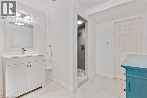 White vanity with a single basin and chrome faucet, framed mirror with sconce lighting, walk-in shower with tile surround, and light-toned tile flooring - 7 Shadywood Lane, Cambridge, ON 