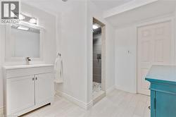 White vanity with a single basin and chrome faucet, framed mirror with sconce lighting, walk-in shower with tile surround, and light-toned tile flooring - 