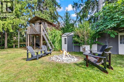 Expansive backyard featuring a stone fire pit, wood-built play structure, and two storage sheds - 7 Shadywood Lane, Cambridge, ON 